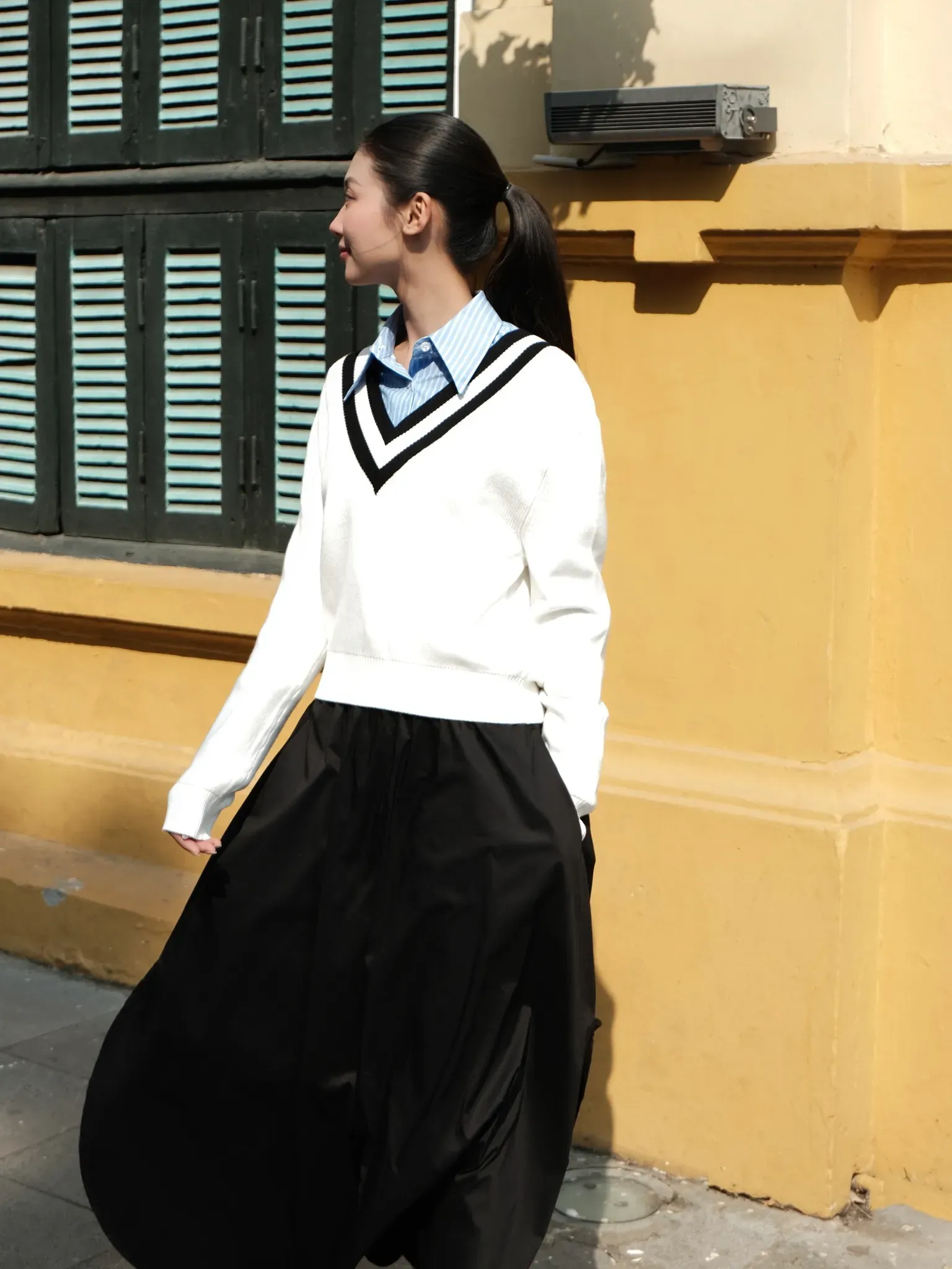 Outfit kết hợp áo len trắng với kiểu dáng trẻ trung và chân váy đen dài, mang đến sự thanh lịch và tối giản (Nguồn: Routine)